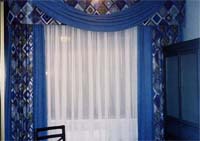 Firanka z woalu, dekoracja wielowarstwowa: zasony dekoracyjne (wzorzyste), pod nimi z gadkiej niebieskiej tkaniny zasony do zasaniania, lambrekin sztywny(wzorzysty) z podwieszonym ukiem z tkaniny gadkiej